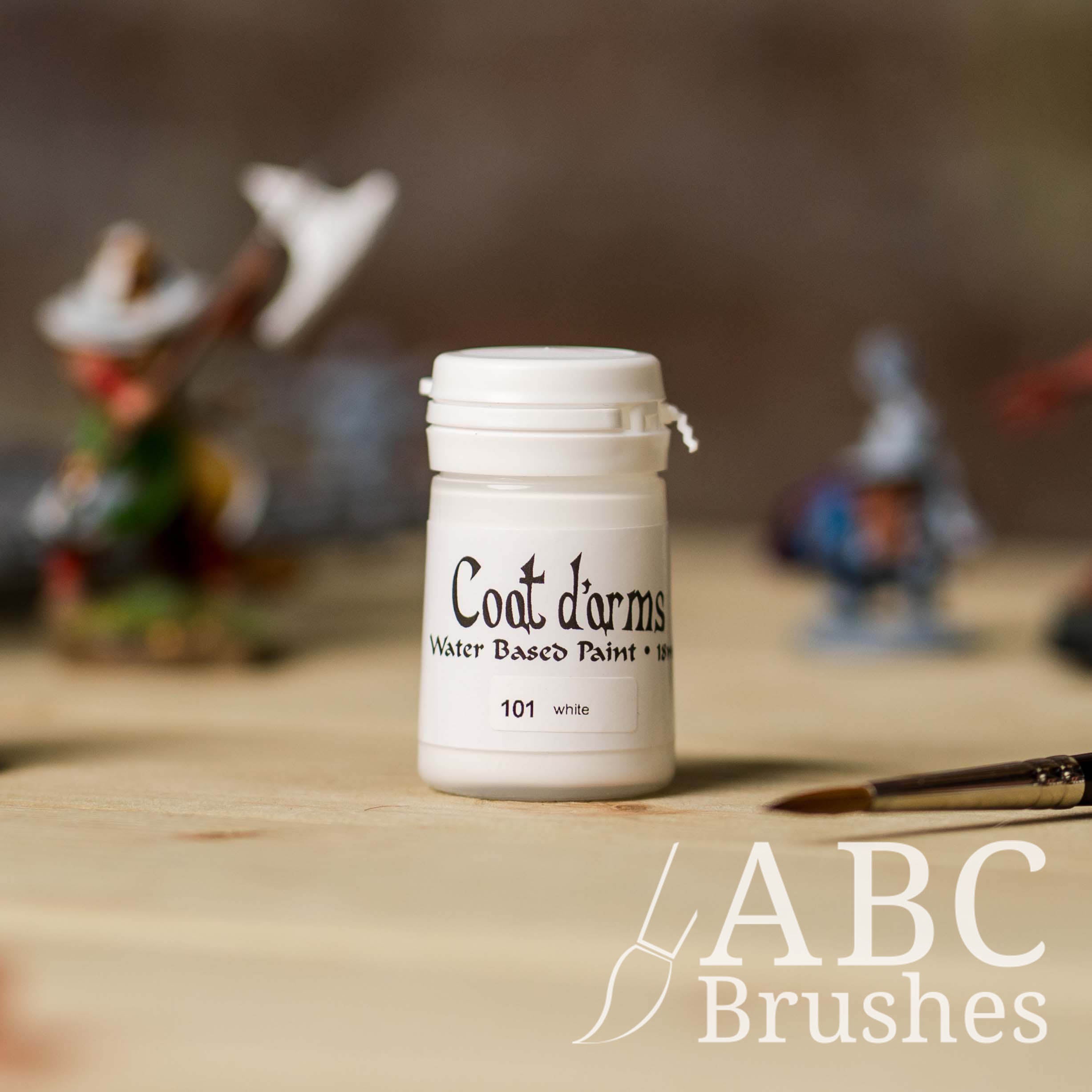Bottle of Coat d'Arms acrylic paint in the colour White, with various wargaming models and an ABC paintbrush in the background, on a wooden surface.