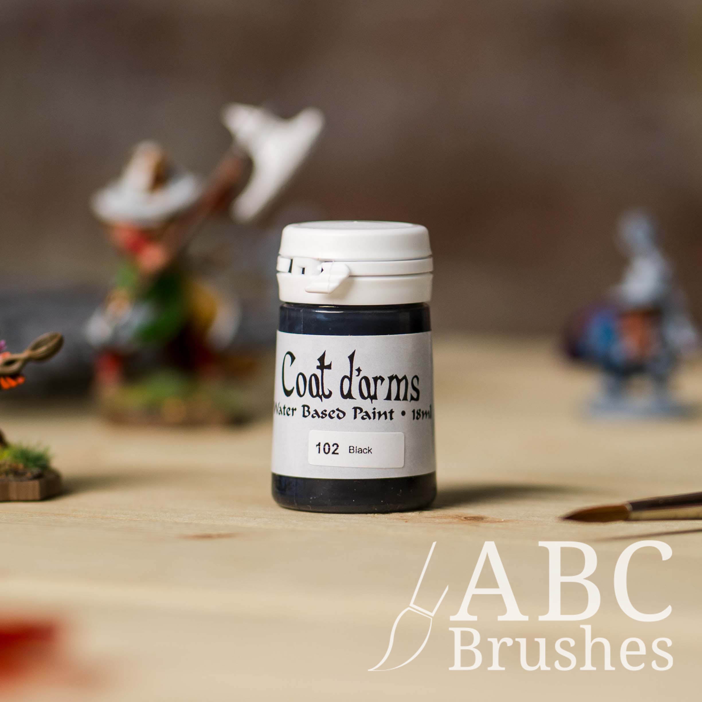 Bottle of Coat d'Arms acrylic paint in the colour Black, with various wargaming models and an ABC paintbrush in the background, on a wooden surface.