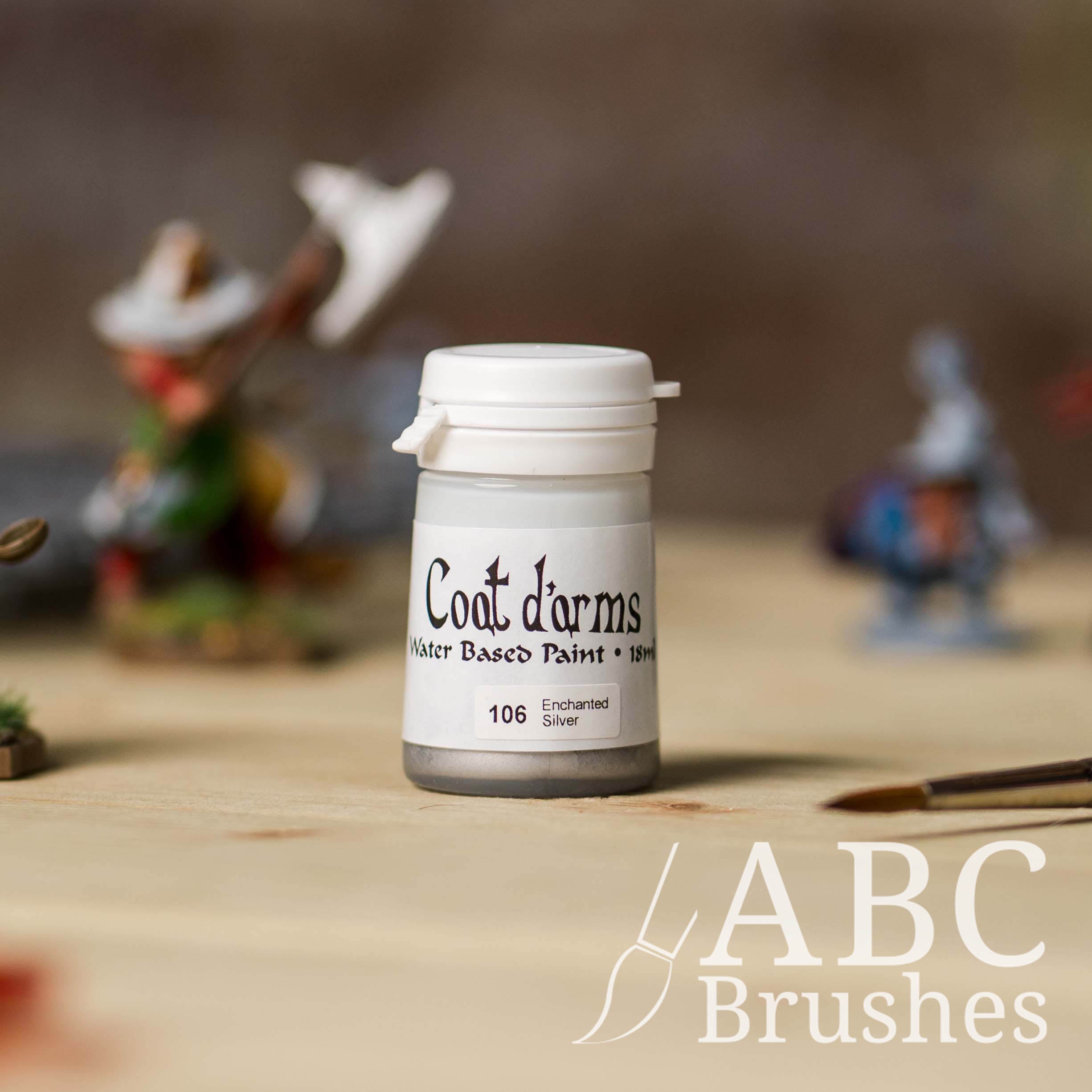 Bottle of Coat d'Arms acrylic paint in the colour Enchanted Silver, with various wargaming models and an abc paintbrush in the background, on a wooden surface.