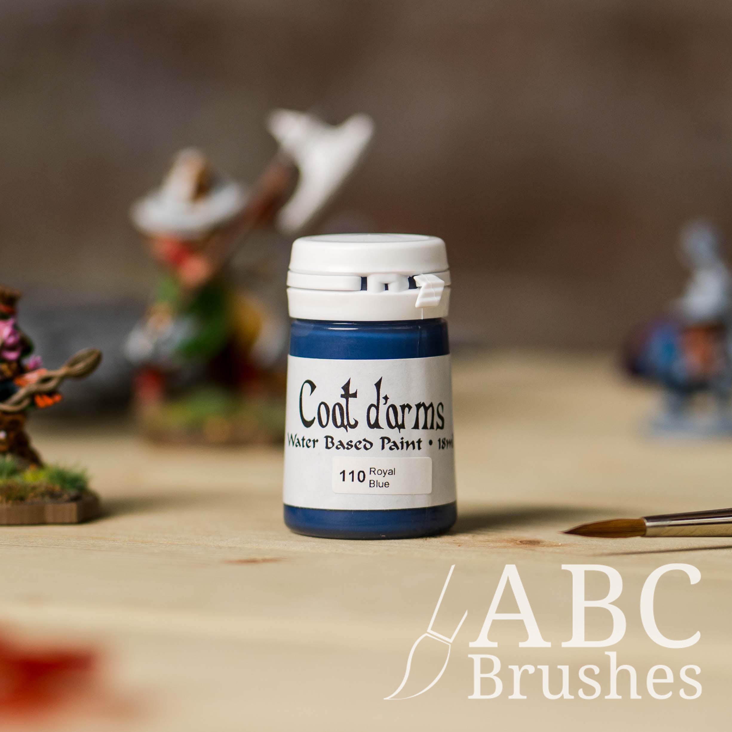Bottle of Coat d'Arms acrylic paint in the colour Royal Blue, with various wargaming models and an abc paintbrush in the background, on a wooden surface.