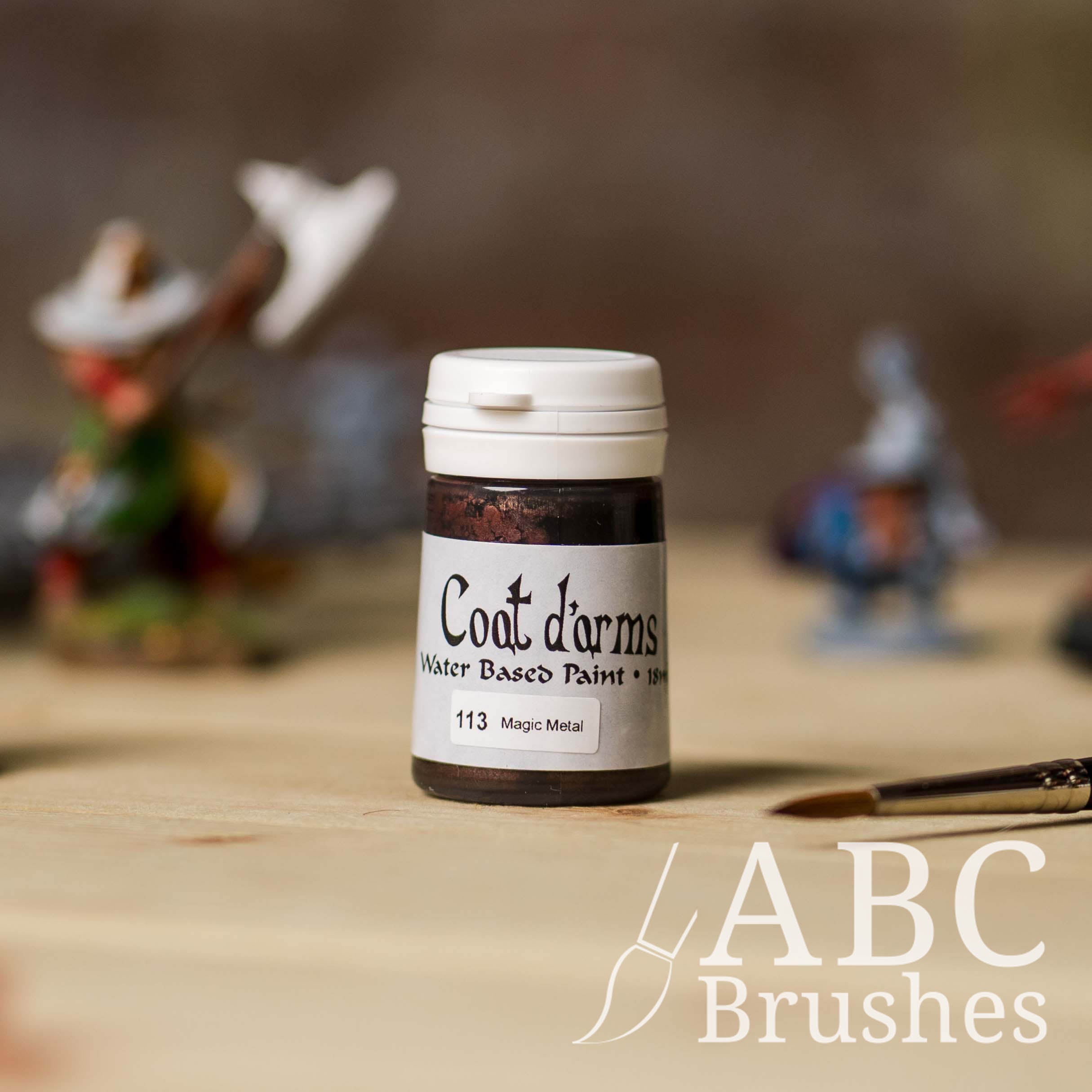 Bottle of Coat d'Arms acrylic paint in the colour Magic Metal, with various wargaming models and an abc paintbrush in the background, on a wooden surface.