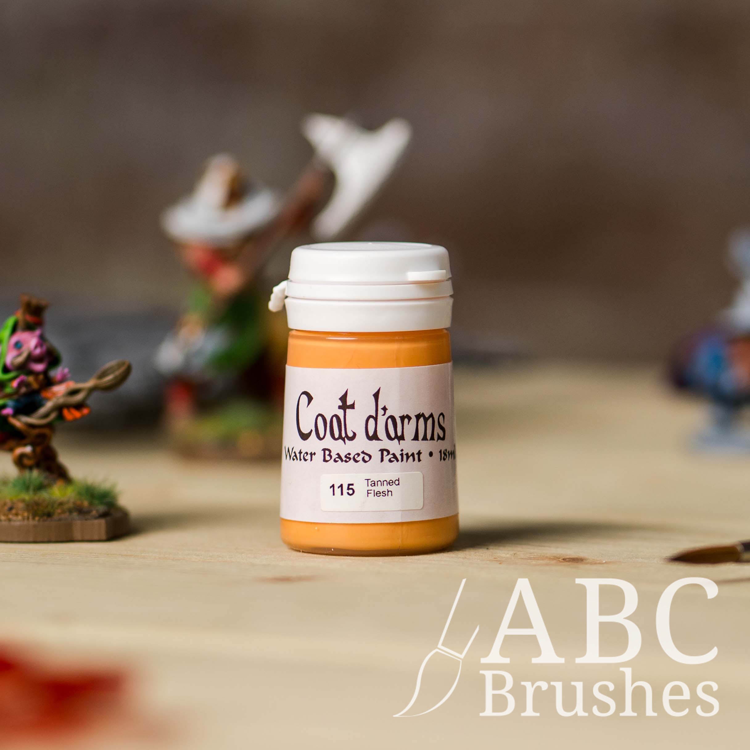 Bottle of Coat d'Arms acrylic paint in the colour Tanned Flesh, with various wargaming models and an abc paintbrush in the background, on a wooden surface.