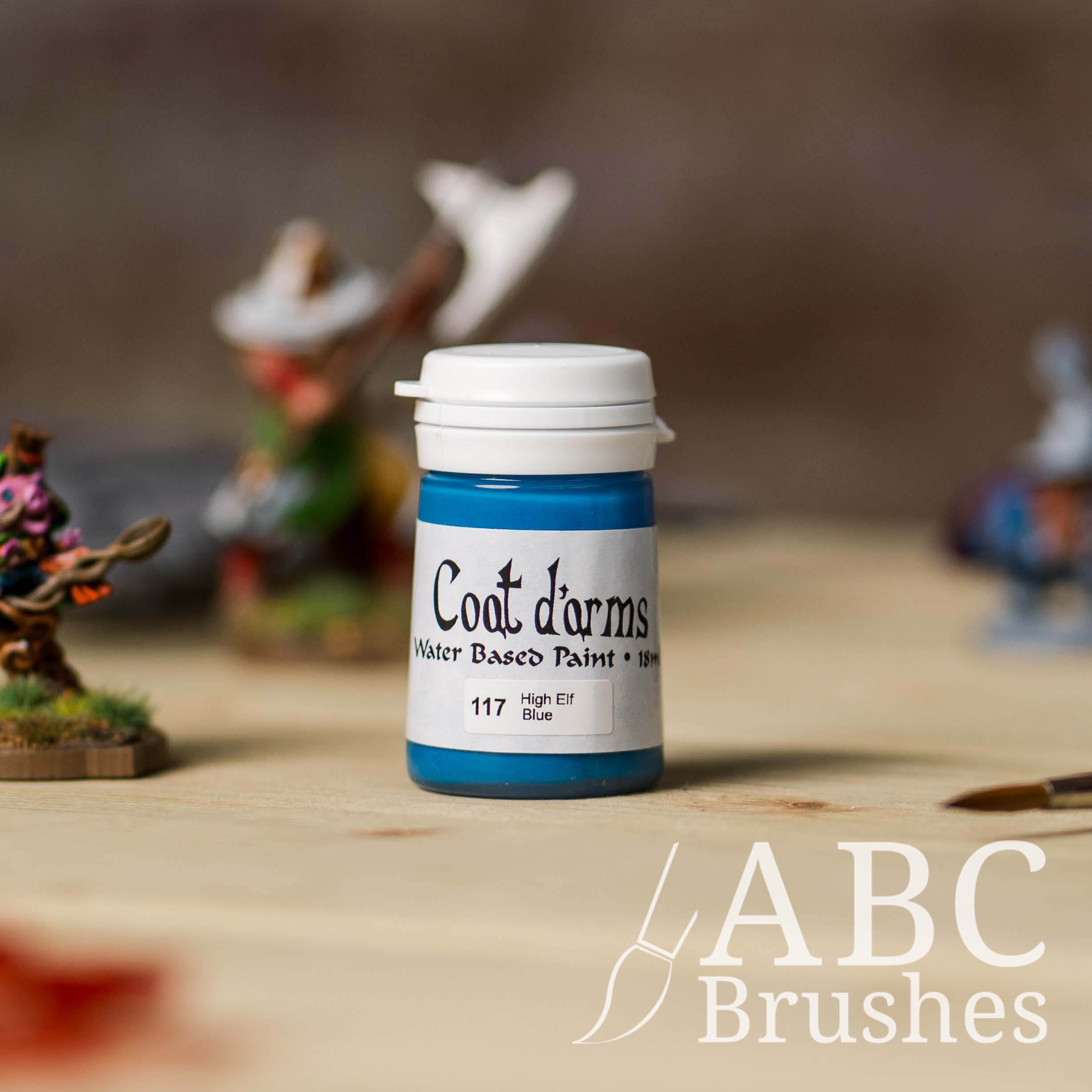 Bottle of Coat d'Arms acrylic paint in the colour High Elf Blue, with various wargaming models and an abc paintbrush in the background, on a wooden surface.