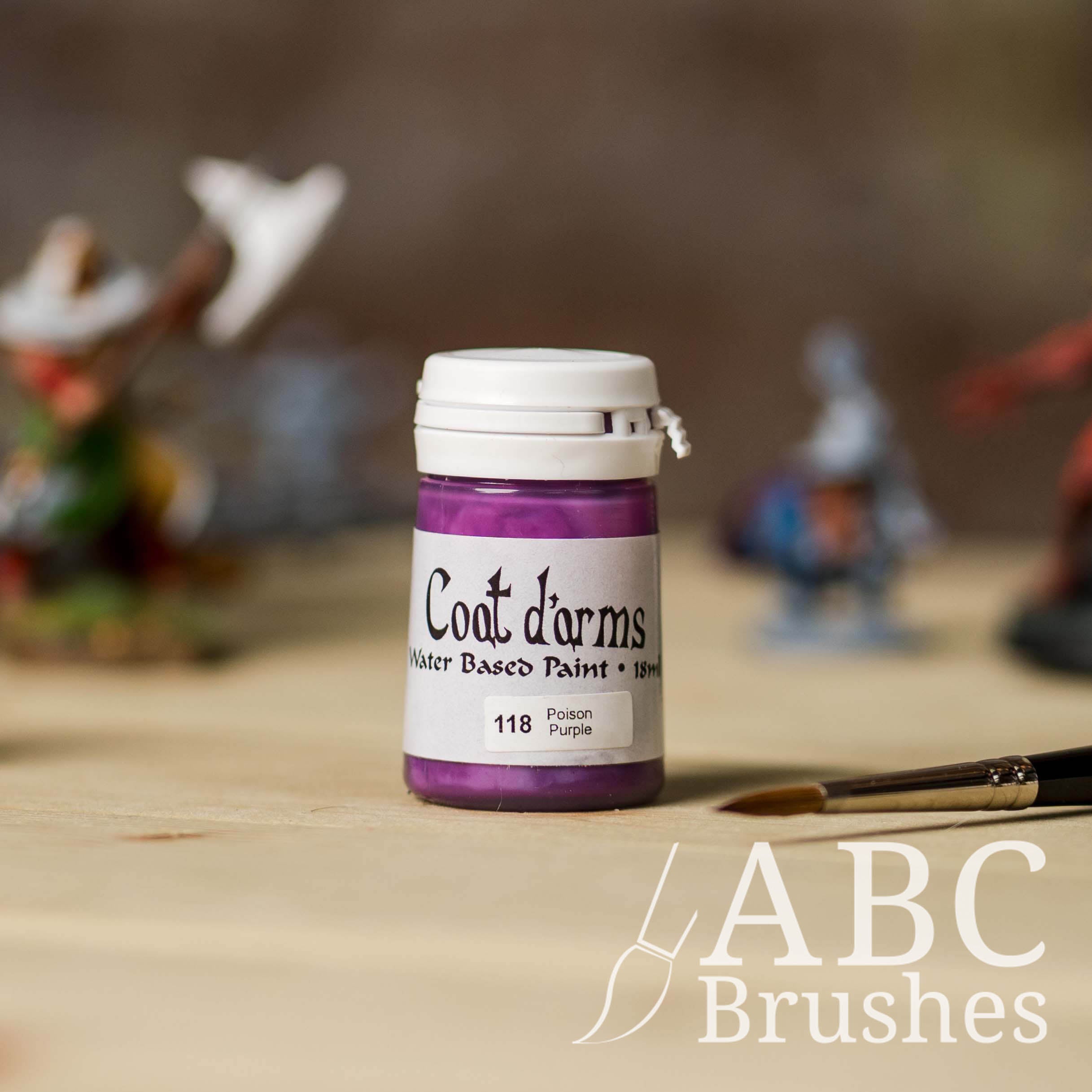 Bottle of Coat d'Arms acrylic paint in the colour Poison Purple, with various wargaming models and an abc paintbrush in the background, on a wooden surface.