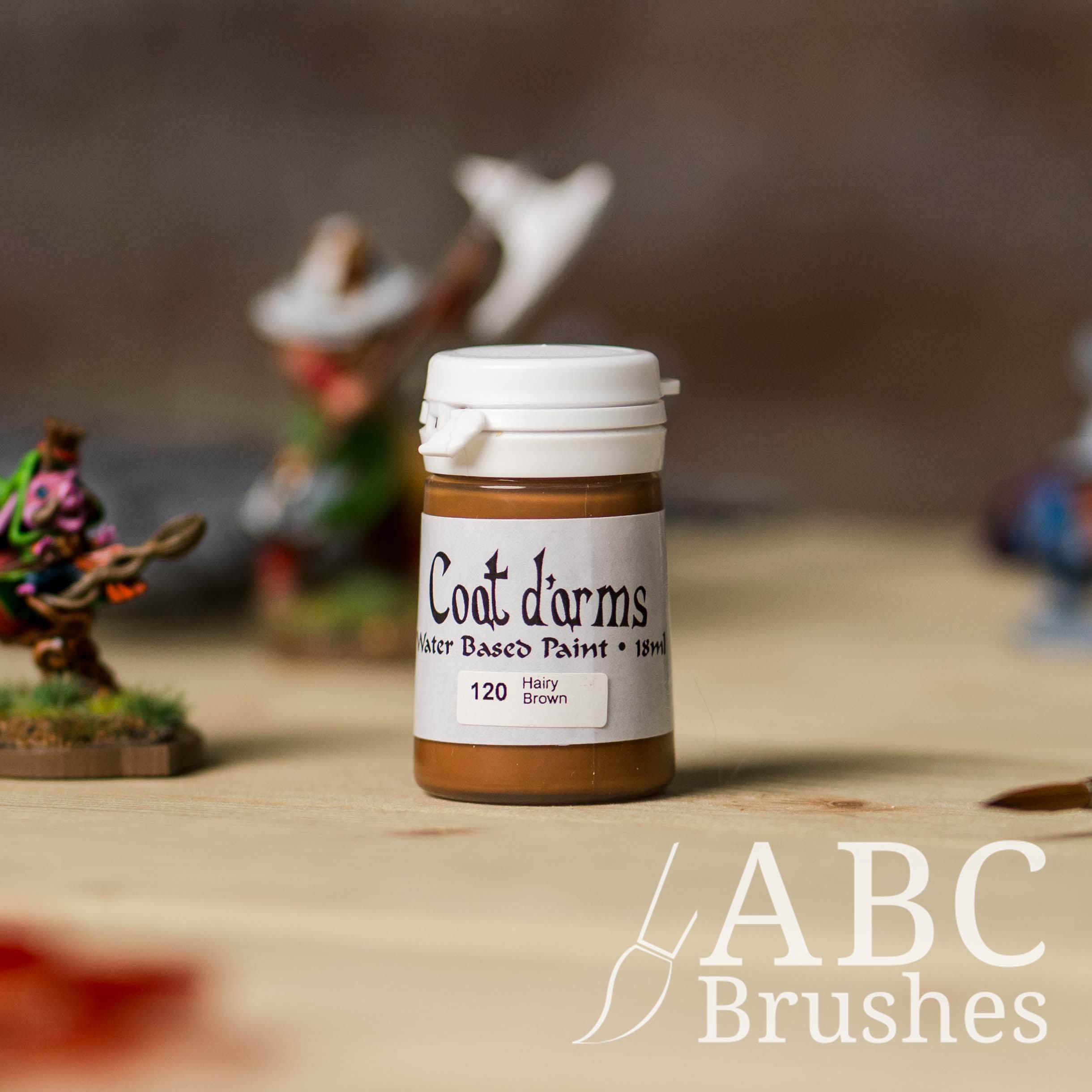 Bottle of Coat d'Arms acrylic paint in the colour Hairy Brown, with various wargaming models and an abc paintbrush in the background, on a wooden surface.