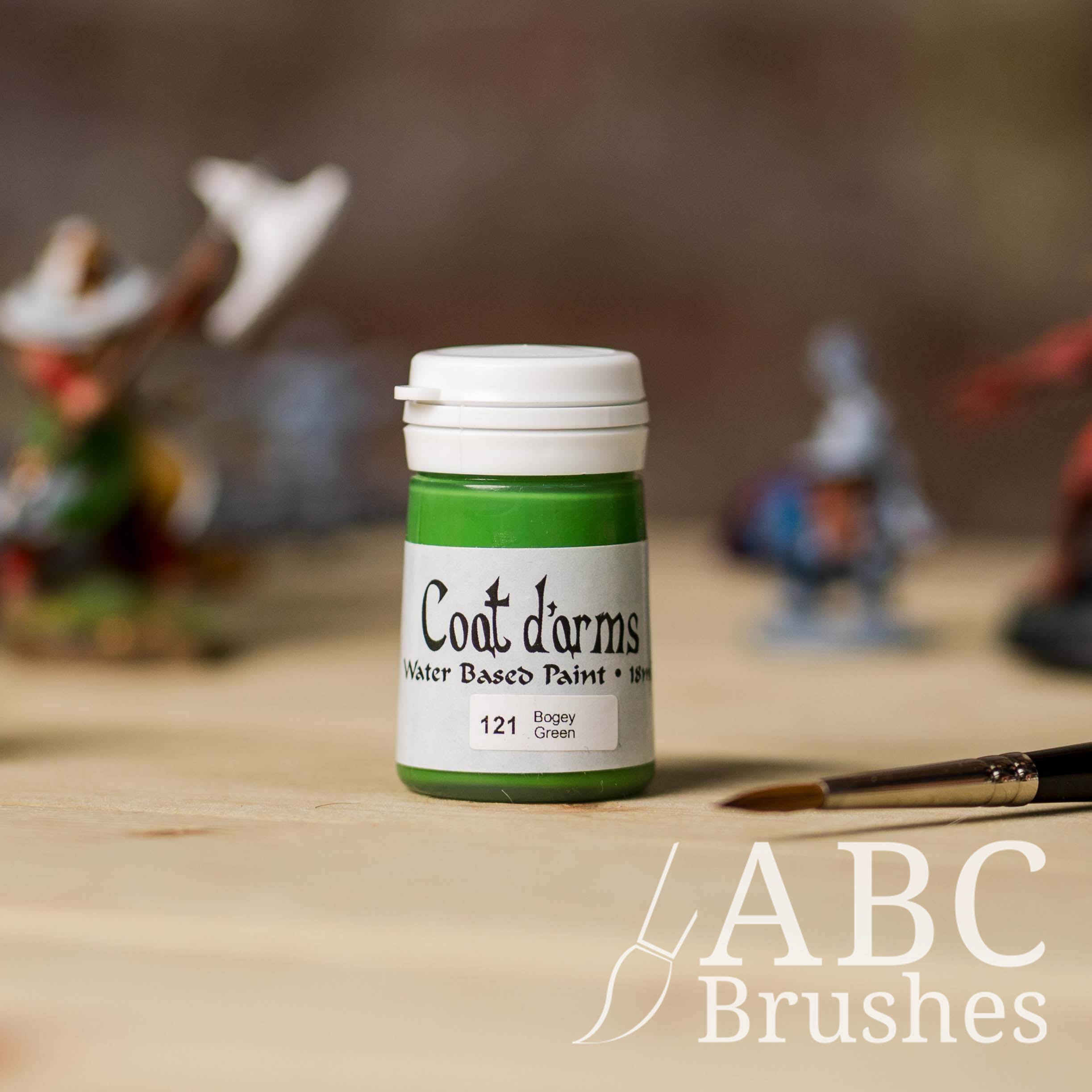 Bottle of Coat d'Arms acrylic paint in the colour Bogey Green, with various wargaming models and an abc paintbrush in the background, on a wooden surface.