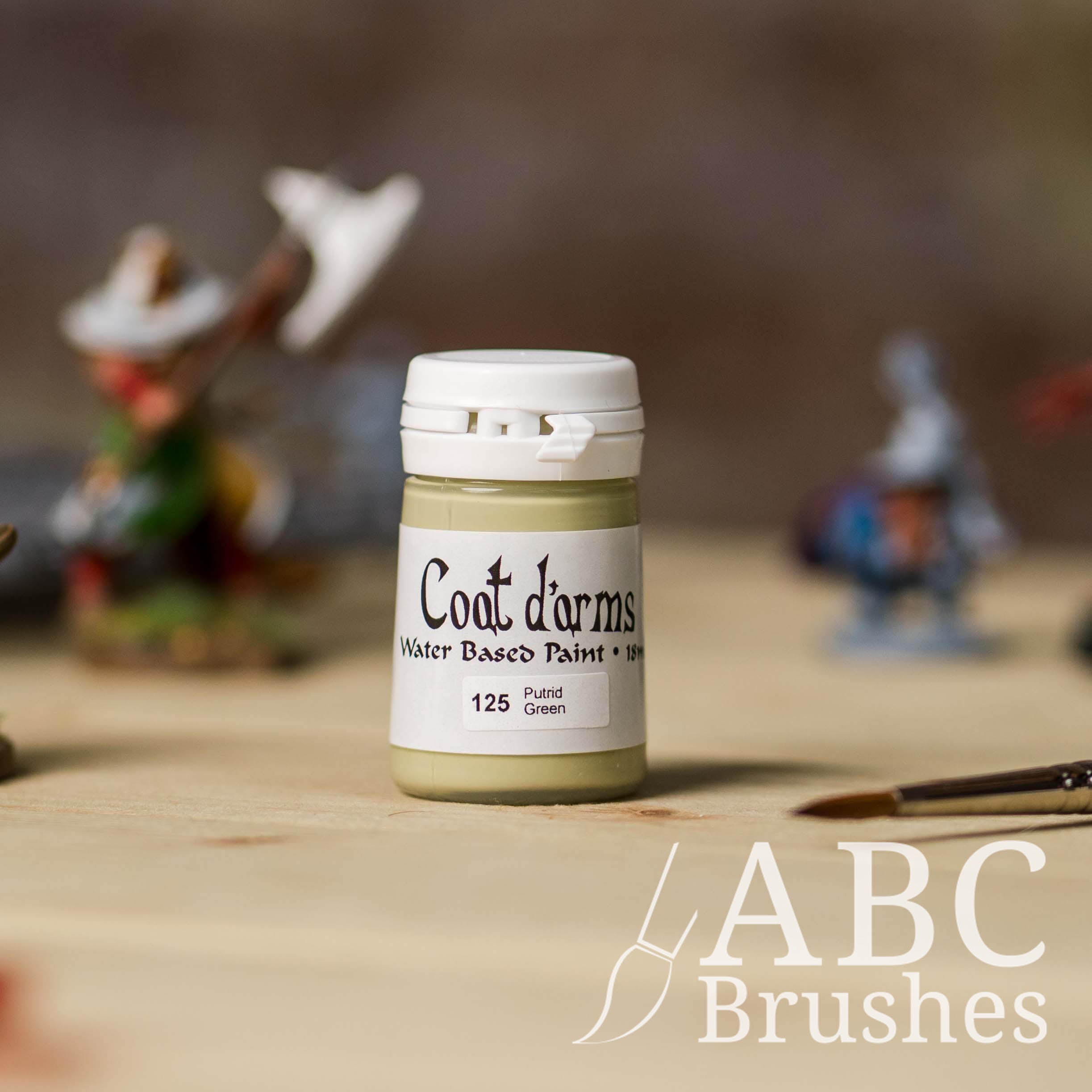 Bottle of Coat d'Arms acrylic paint in the colour Putrid Green, with various wargaming models and an abc paintbrush in the background, on a wooden surface.