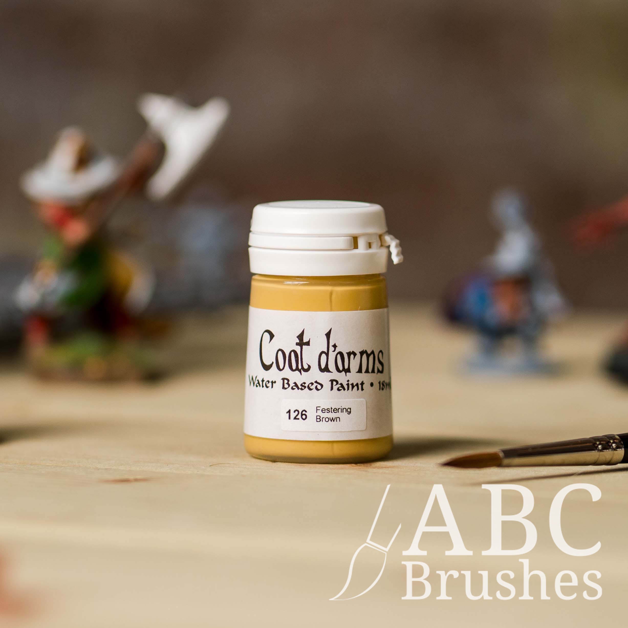 Bottle of Coat d'Arms acrylic paint in the colour Festering Brown, with various wargaming models and an abc paintbrush in the background, on a wooden surface.