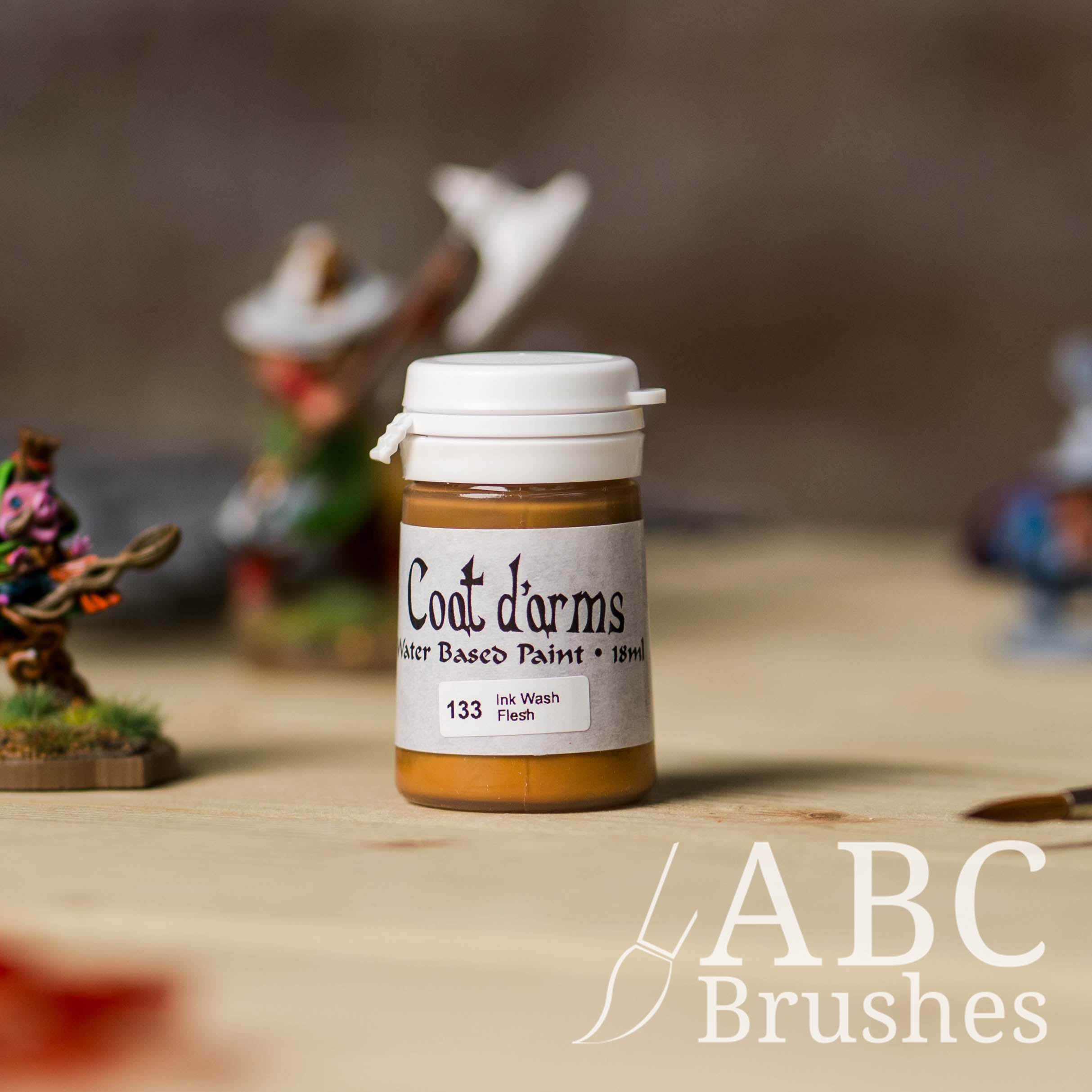Bottle of Coat d'Arms ink wash in the colour Flesh, with various wargaming models and an abc paintbrush in the background, on a wooden surface.