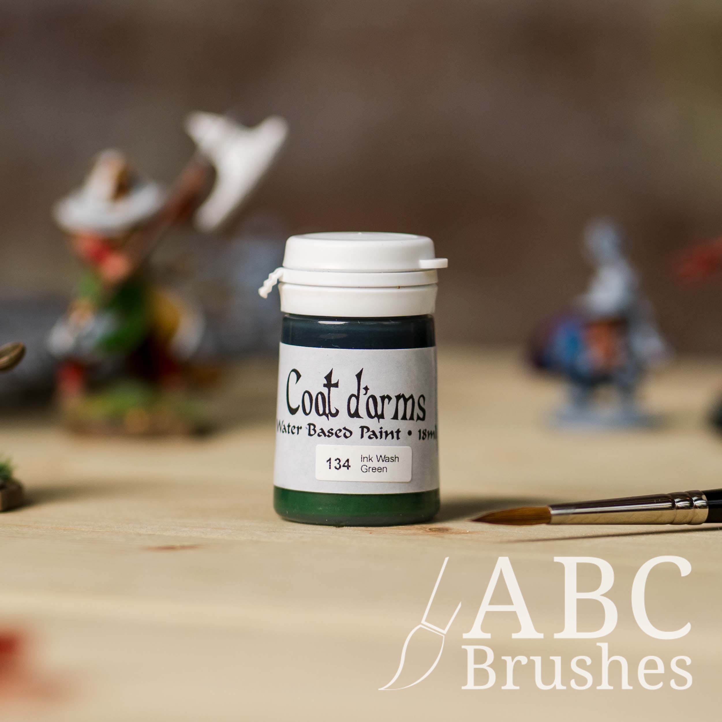 Bottle of Coat d'Arms ink wash in the colour Green, with various wargaming models and an abc paintbrush in the background, on a wooden surface.