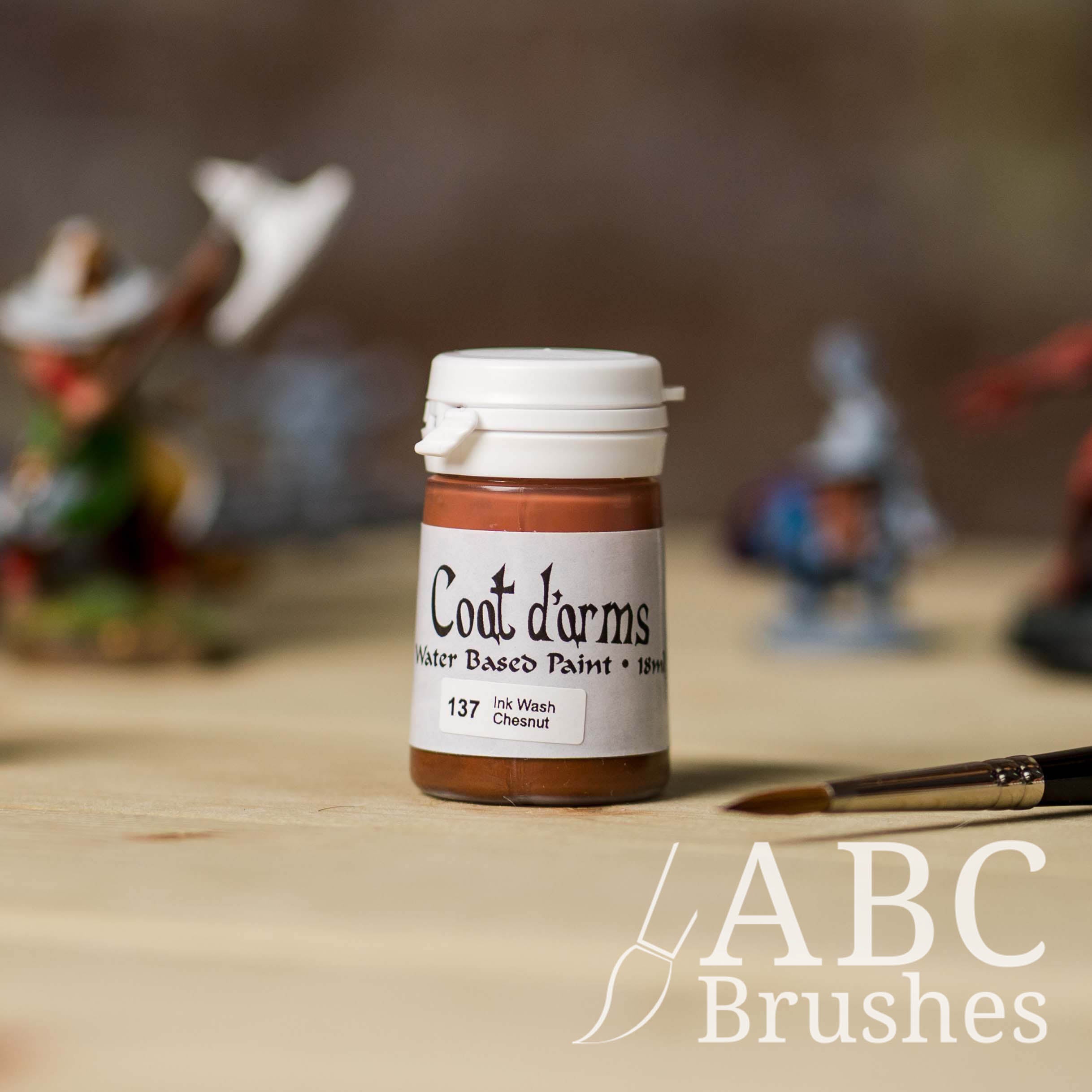 Bottle of Coat d'Arms ink wash in the colour Chesnut, with various wargaming models and an abc paintbrush in the background, on a wooden surface.