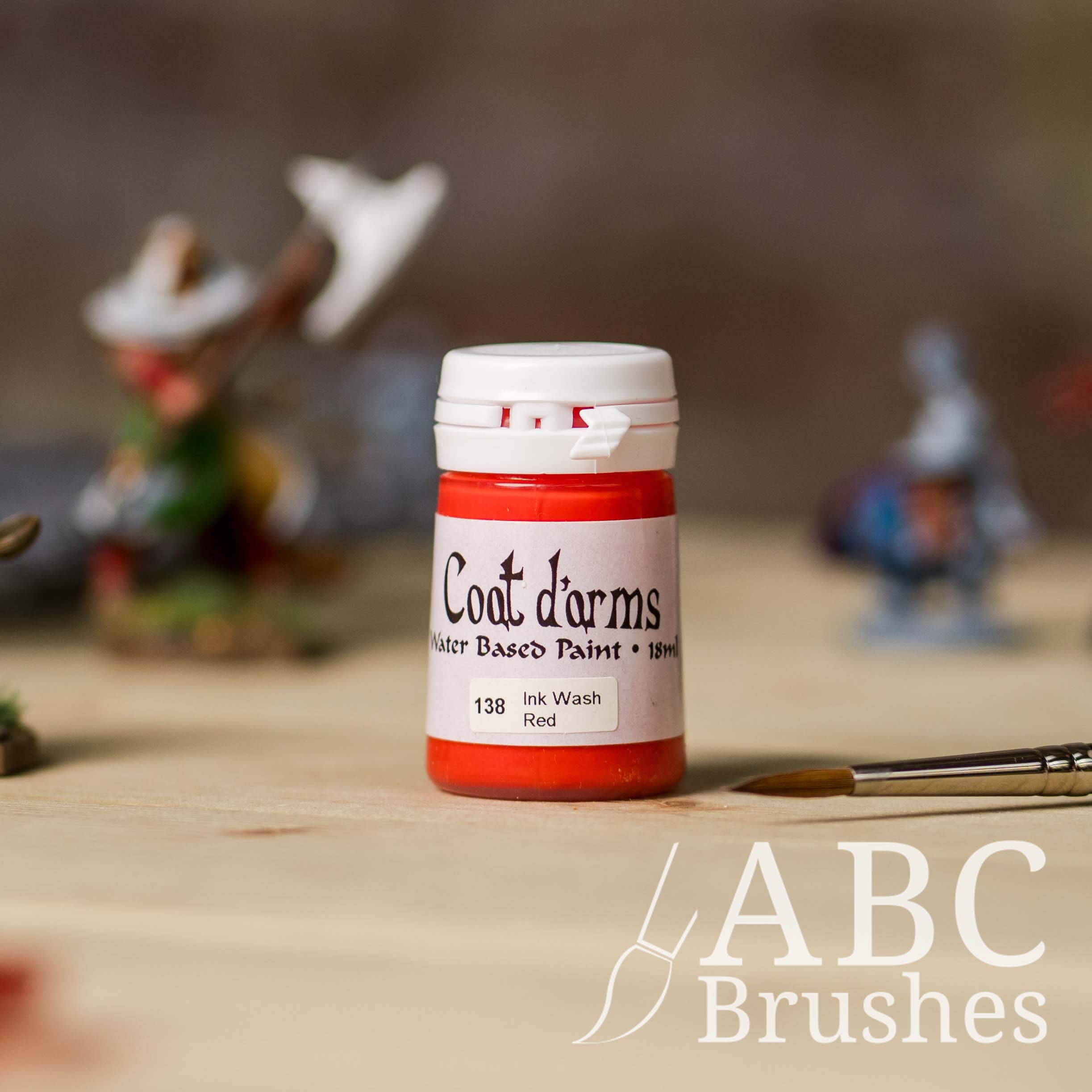 Bottle of Coat d'Arms ink wash in the colour Red, with various wargaming models and an abc paintbrush in the background, on a wooden surface.