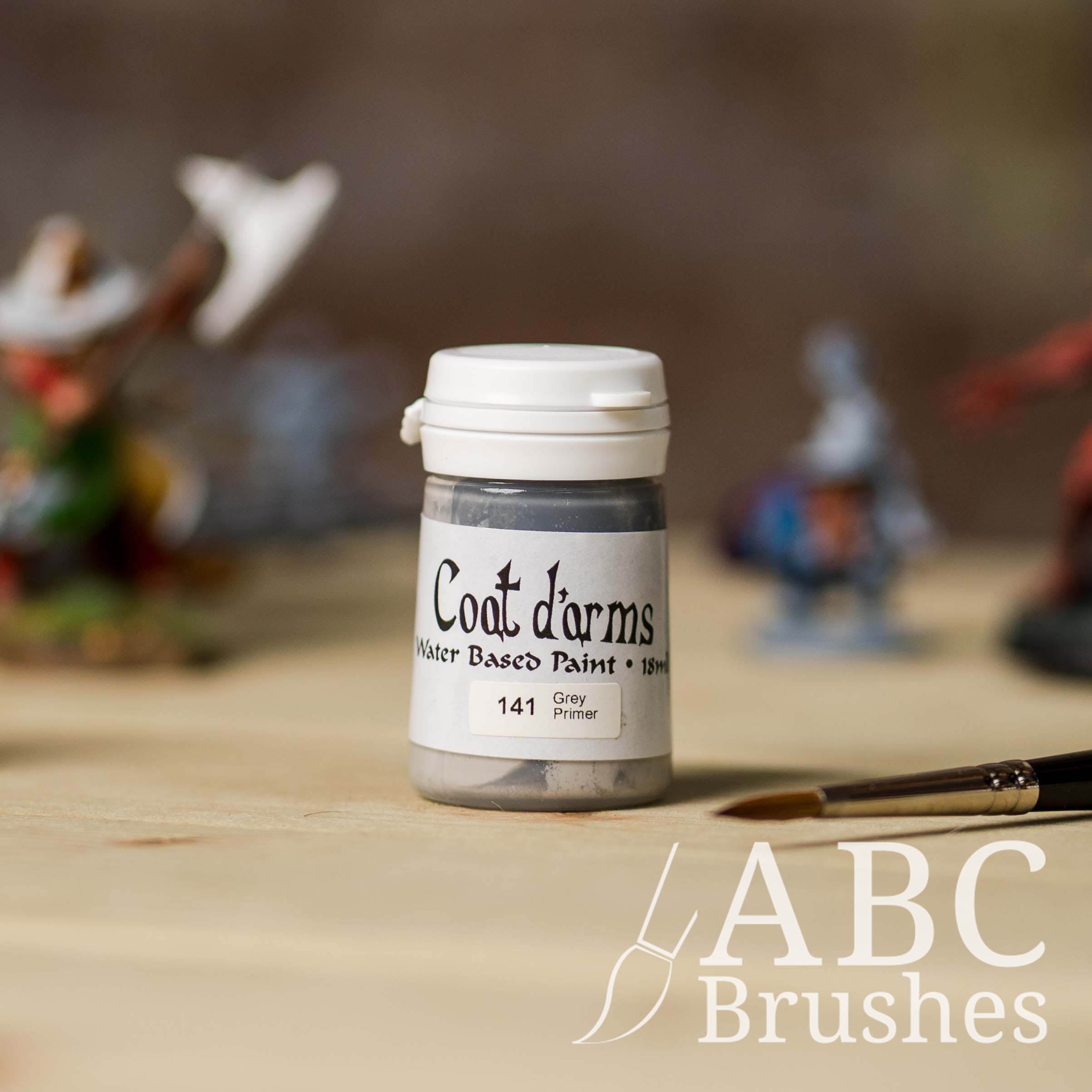 Bottle of Coat d'Arms Grey Acrylic Primer, with various wargaming models and an abc paintbrush in the background, on a wooden surface.