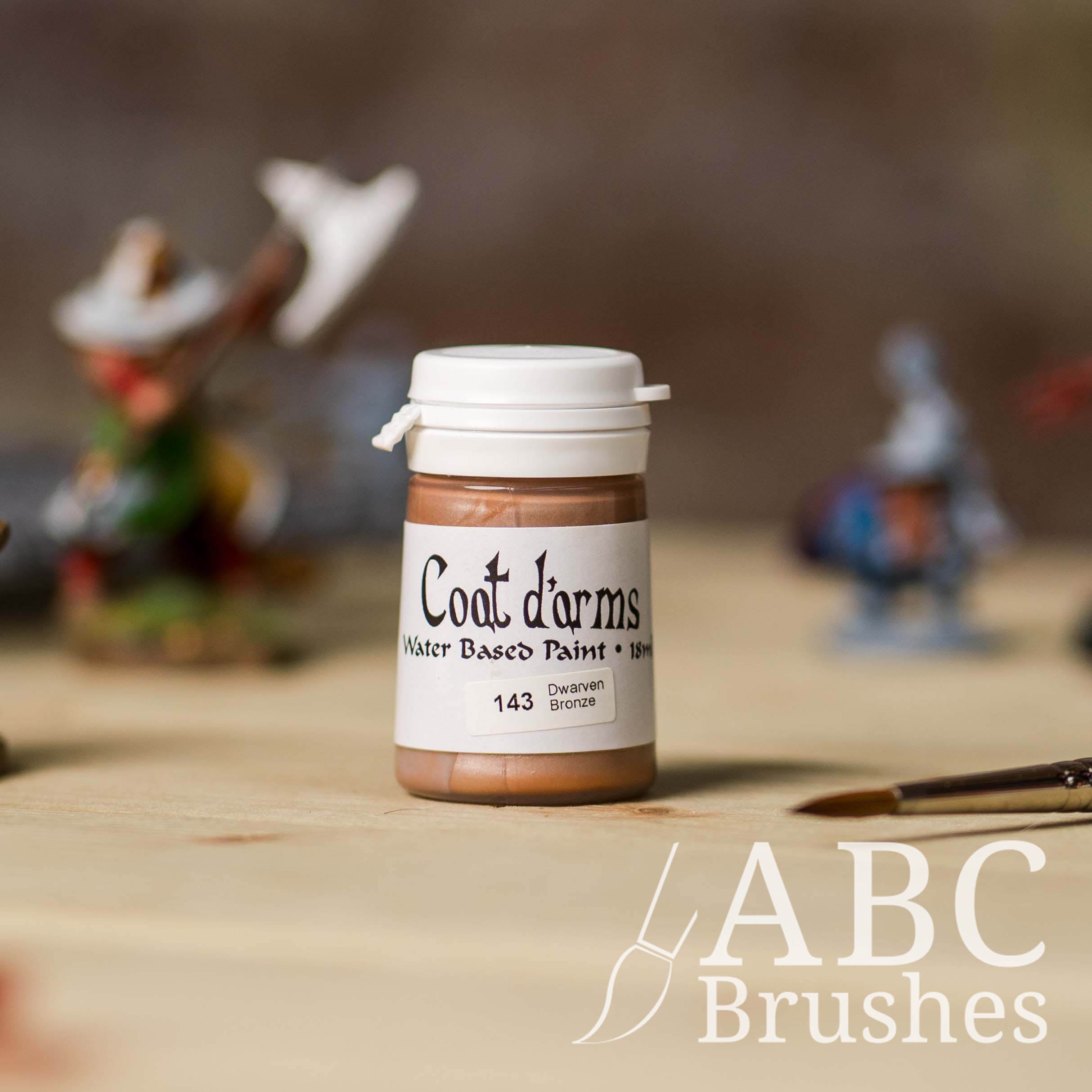 Bottle of Coat d'Arms paint in the colour Dwarven Bronze, with various wargaming models and an abc paintbrush in the background, on a wooden surface.