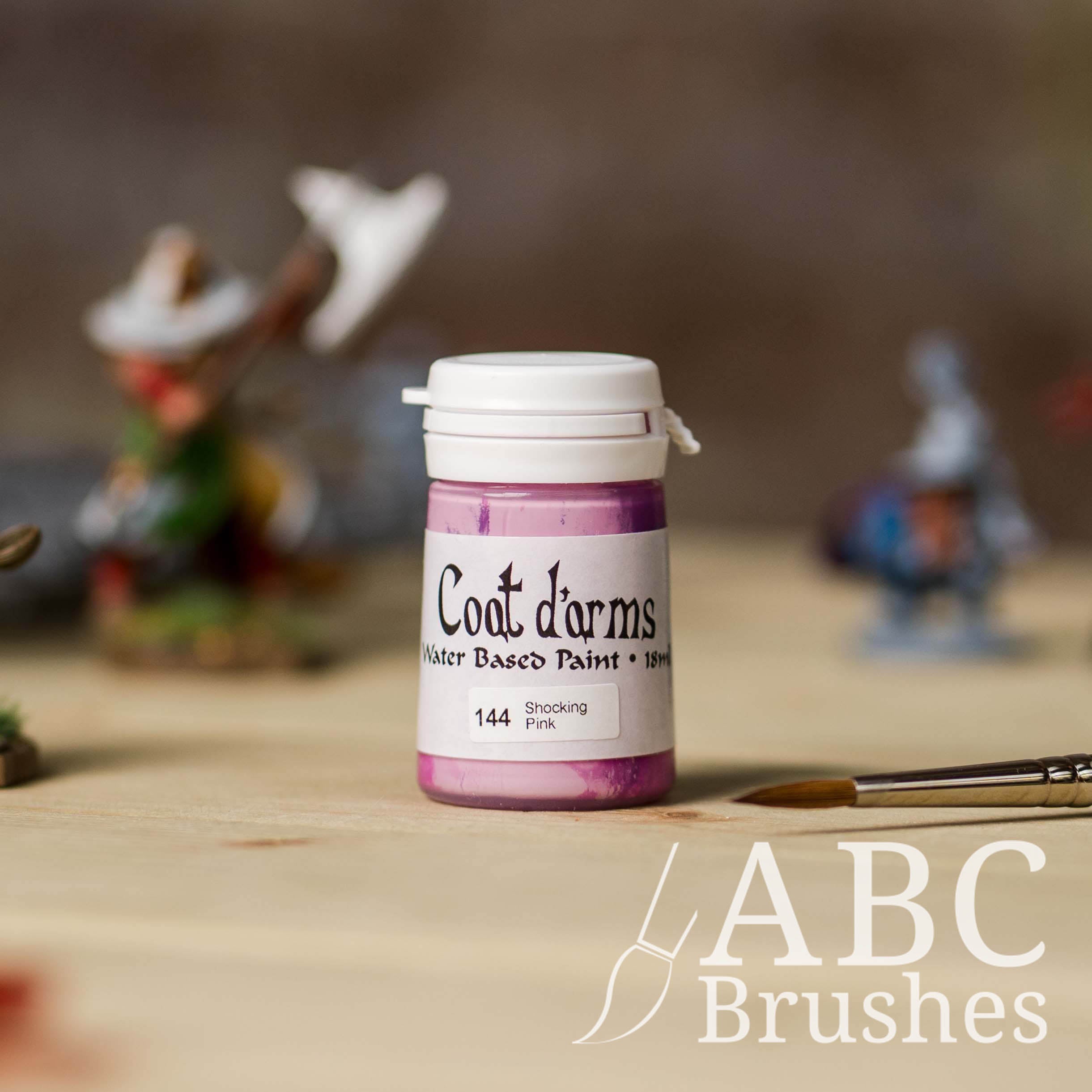Bottle of Coat d'Arms paint in the colour Shocking Pink, with various wargaming models and an abc paintbrush in the background, on a wooden surface.