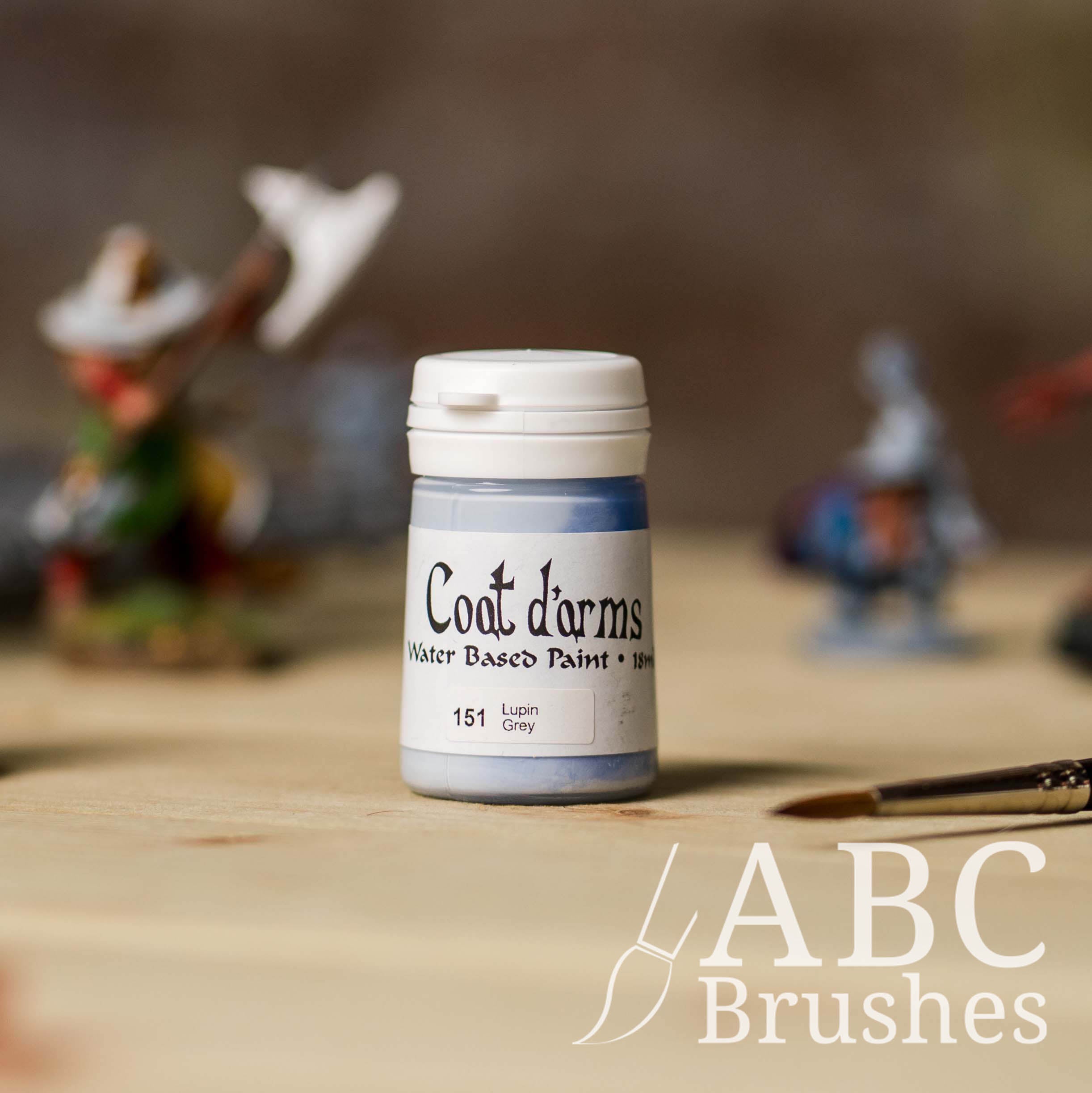 Bottle of Coat d'Arms paint in the colour Lupin Grey, with various wargaming models and an abc paintbrush in the background, on a wooden surface.