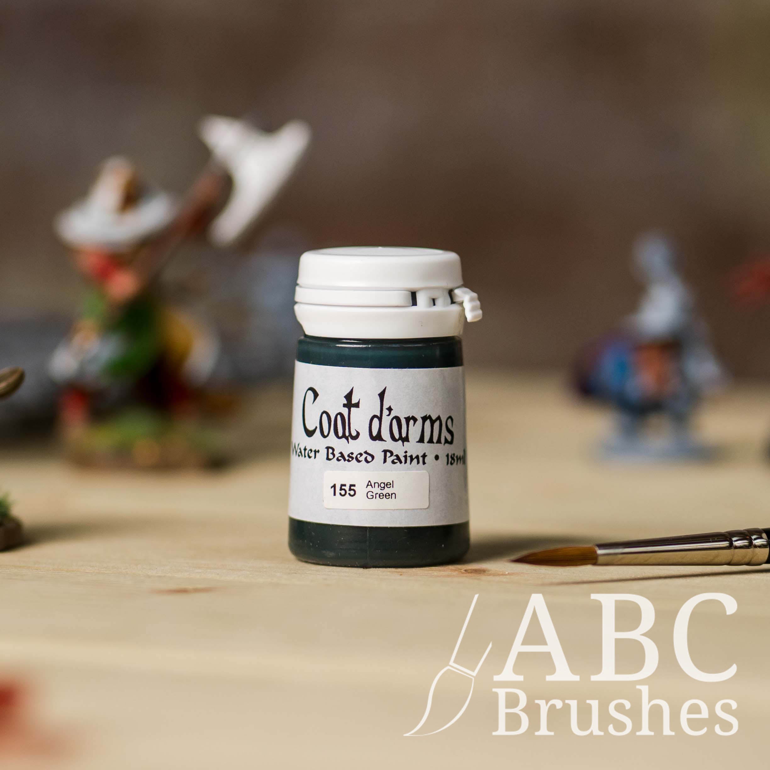 Bottle of Coat d'Arms paint in the colour Angel Green, with various wargaming models and an abc paintbrush in the background, on a wooden surface.