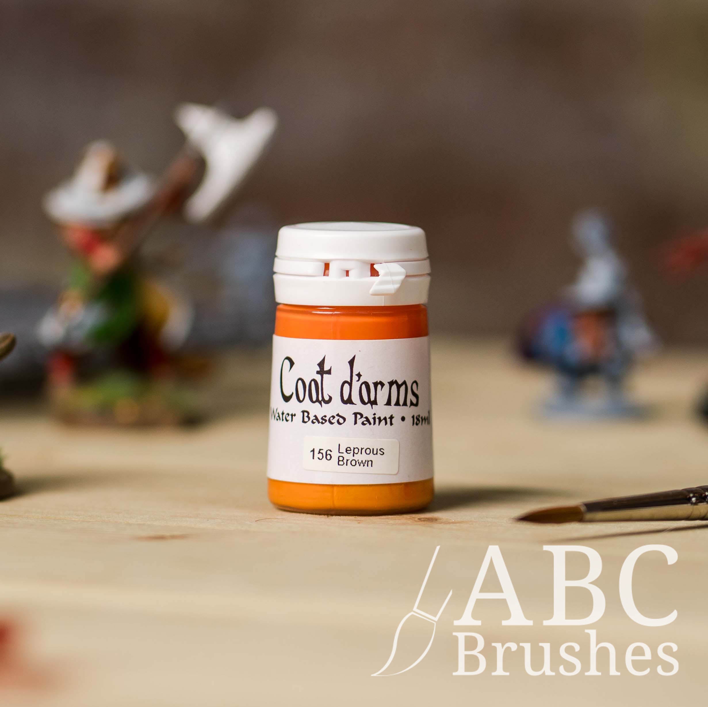 Bottle of Coat d'Arms Acrylic paint in the colour Leprous Brown, with various wargaming models and an abc paintbrush in the background, on a wooden surface.