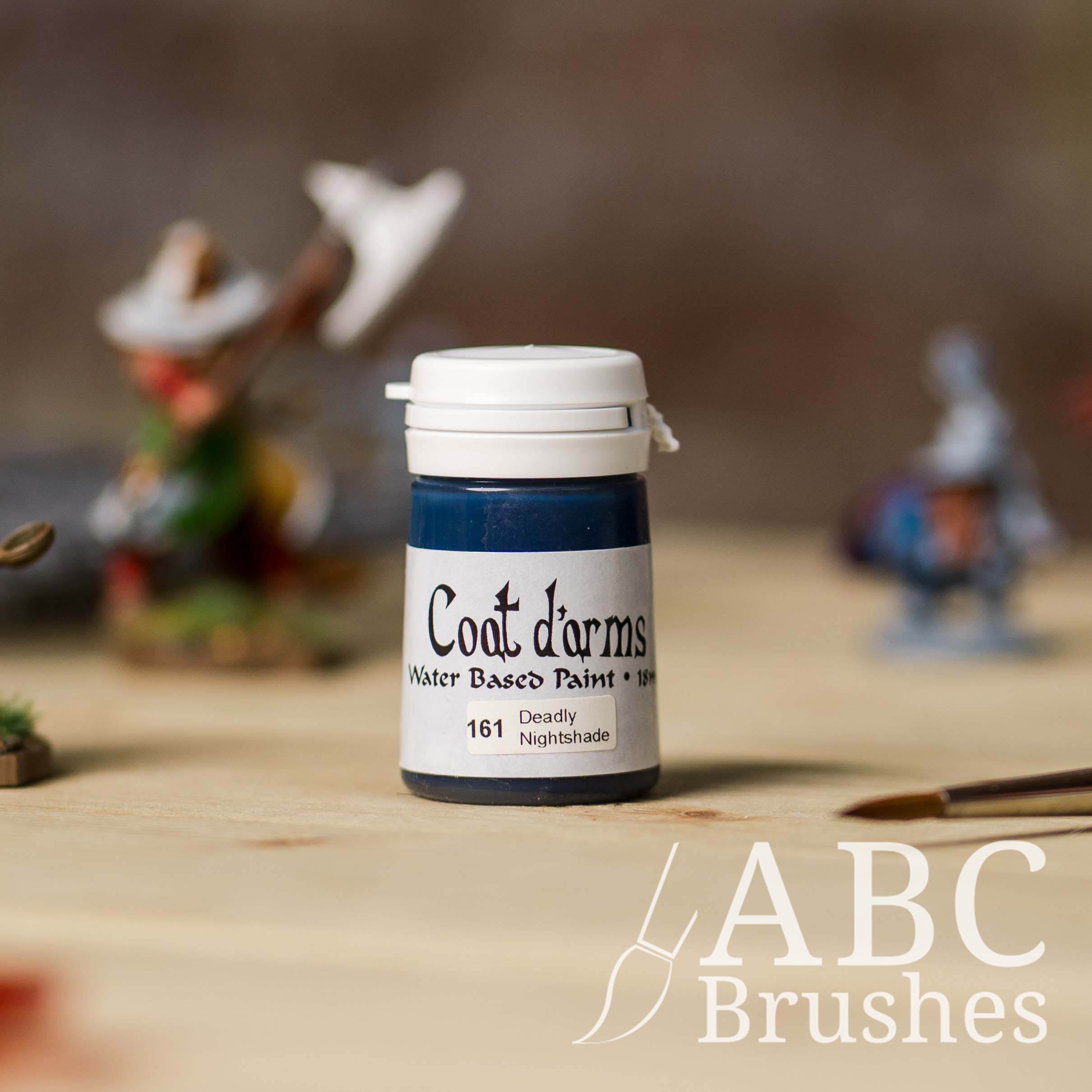 Bottle of Coat d'Arms Acrylic paint in the colour Deadly Nightshade, with various wargaming models and an abc paintbrush in the background, on a wooden surface.