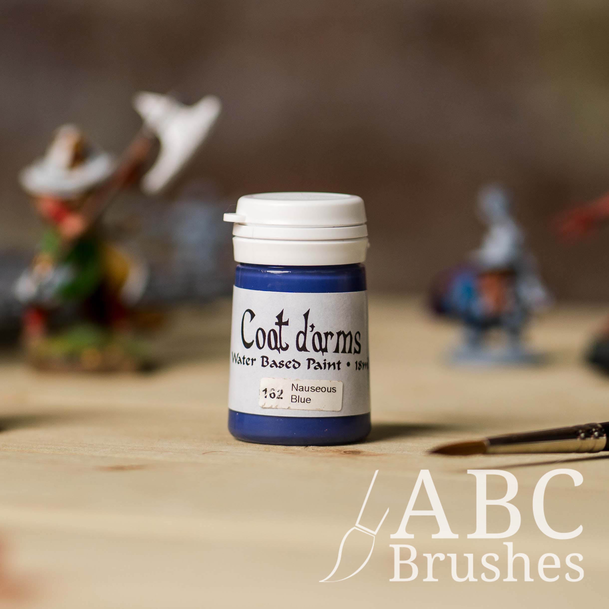 Bottle of Coat d'Arms Acrylic paint in the colour Nauseous Blue, with various wargaming models and an abc paintbrush in the background, on a wooden surface.