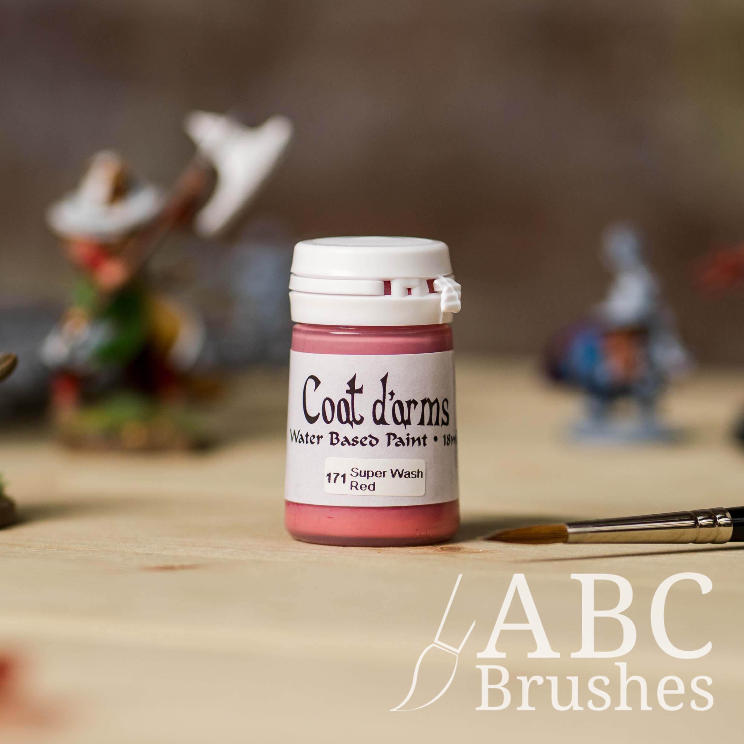 Bottle of Coat d'Arms Super Wash paint in the colour Red, with various wargaming models and an abc paintbrush in the background, on a wooden surface.