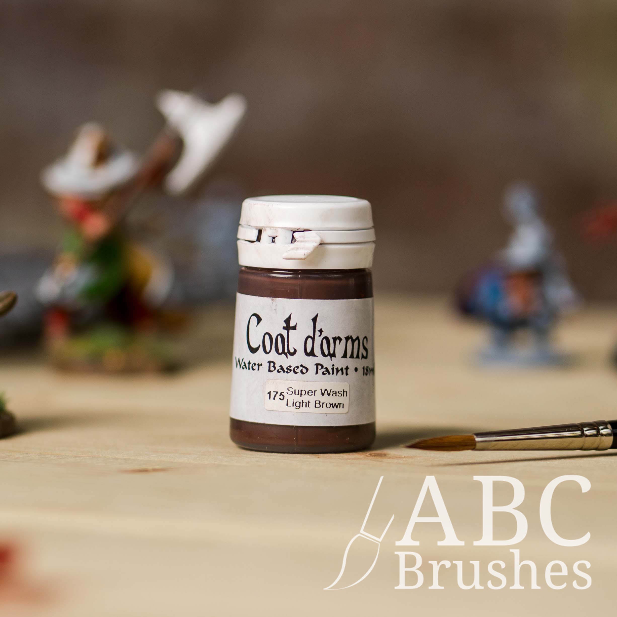 Bottle of Coat d'Arms Super Wash paint in the colour Light Brown, with various wargaming models and an abc paintbrush in the background, on a wooden surface.
