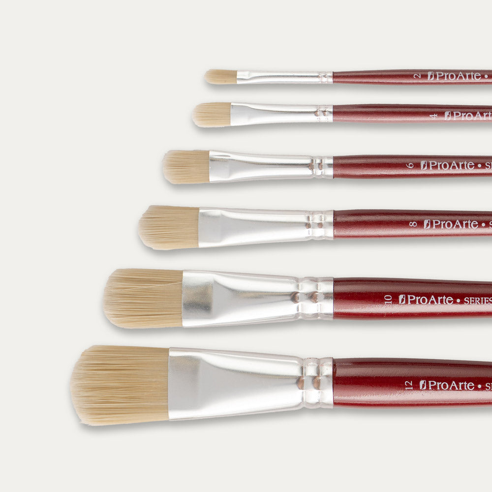 Closeup of the tips of Six Pro Arte Filbert stippler brushes arranged in size order, laid out sideways on a white background.