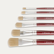 Closeup of the tips of Six Pro Arte Filbert stippler brushes arranged in size order, laid out sideways on a white background.