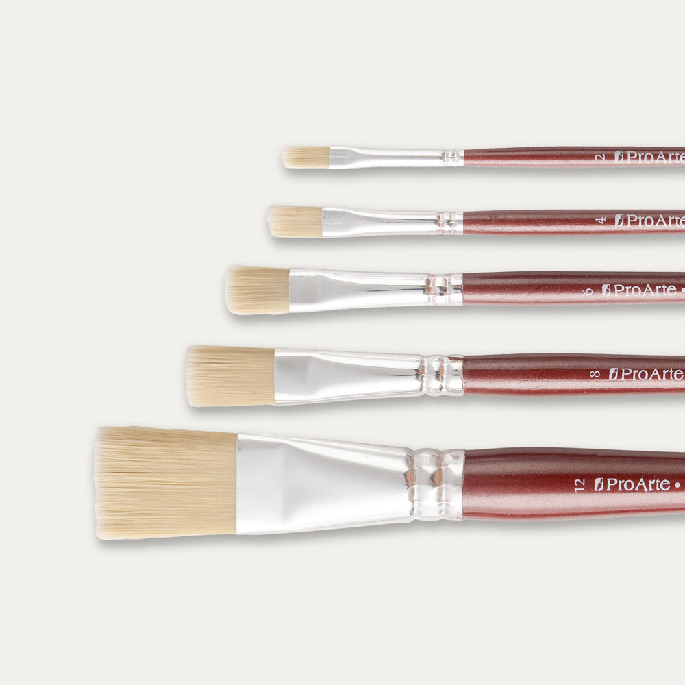 Closeup of the tips of Five Pro Arte Dry Flat brushes arranged in size order, laid out sideways on a white background.