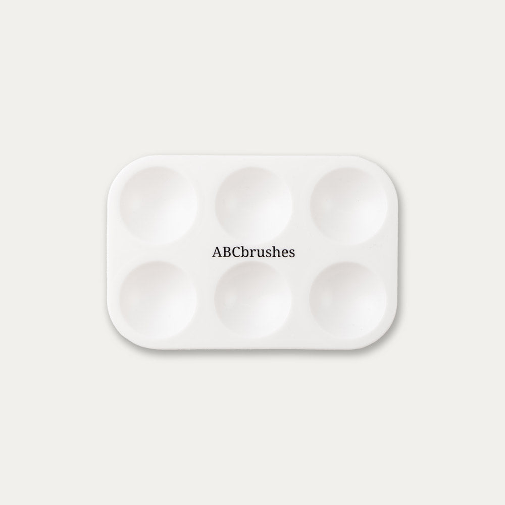 White paint palette with 'ABCbrushes' written on the centre, on a light gray background