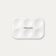 White paint palette with 'ABCbrushes' written on the centre, on a light gray background