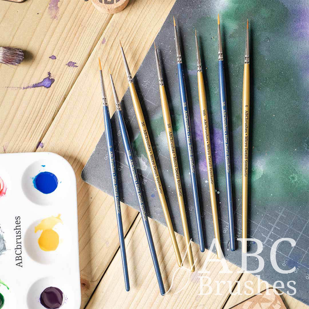 ABC Brushes All Media Micro Detail Synthetic brush range laid out on a paint covered cutting mat and next to a paint palette.