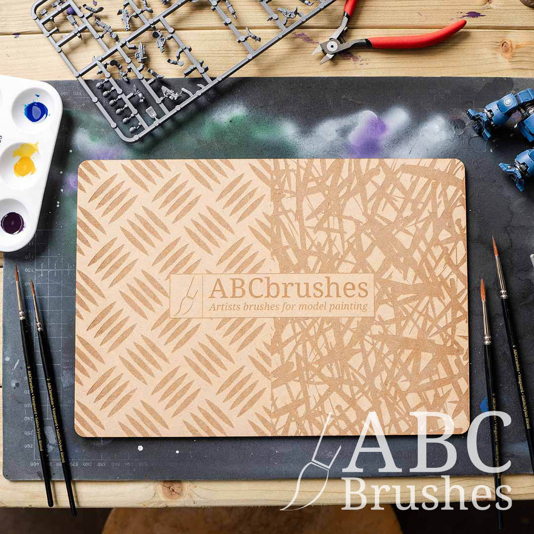 ABC Brushes dry brush board on a paint covered cutting board, surrounded by various miniature painting supplies. 
