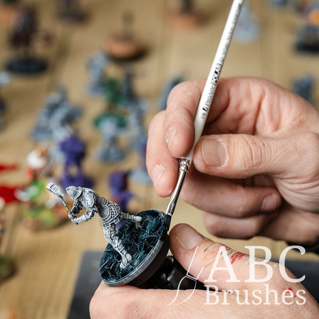 Using a Pro Arte White Nylon flat paint brush to paint the base of a miniature in dark blue paint. 