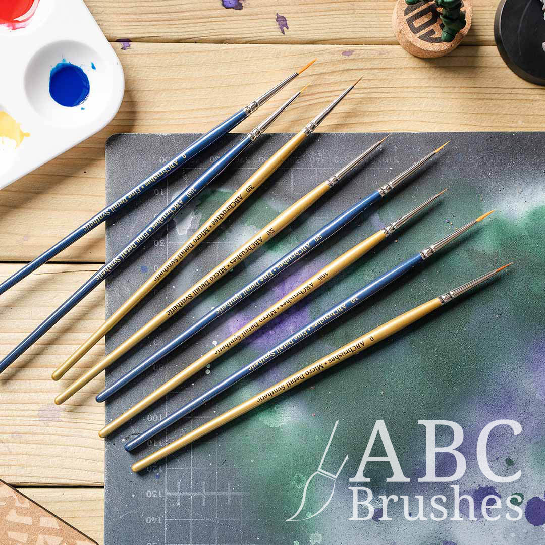 ABC Brushes All Media Micro Detail Synthetic brush range laid out on a paint covered cutting mat and next to a paint palette.