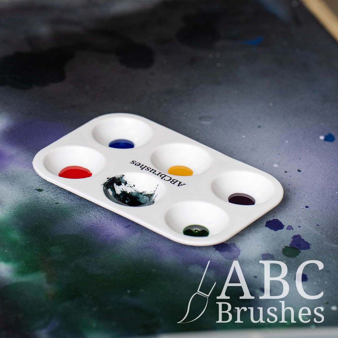 ABC Brushes paint palette filled with various coloured acrylic paints, on a paint covered background.