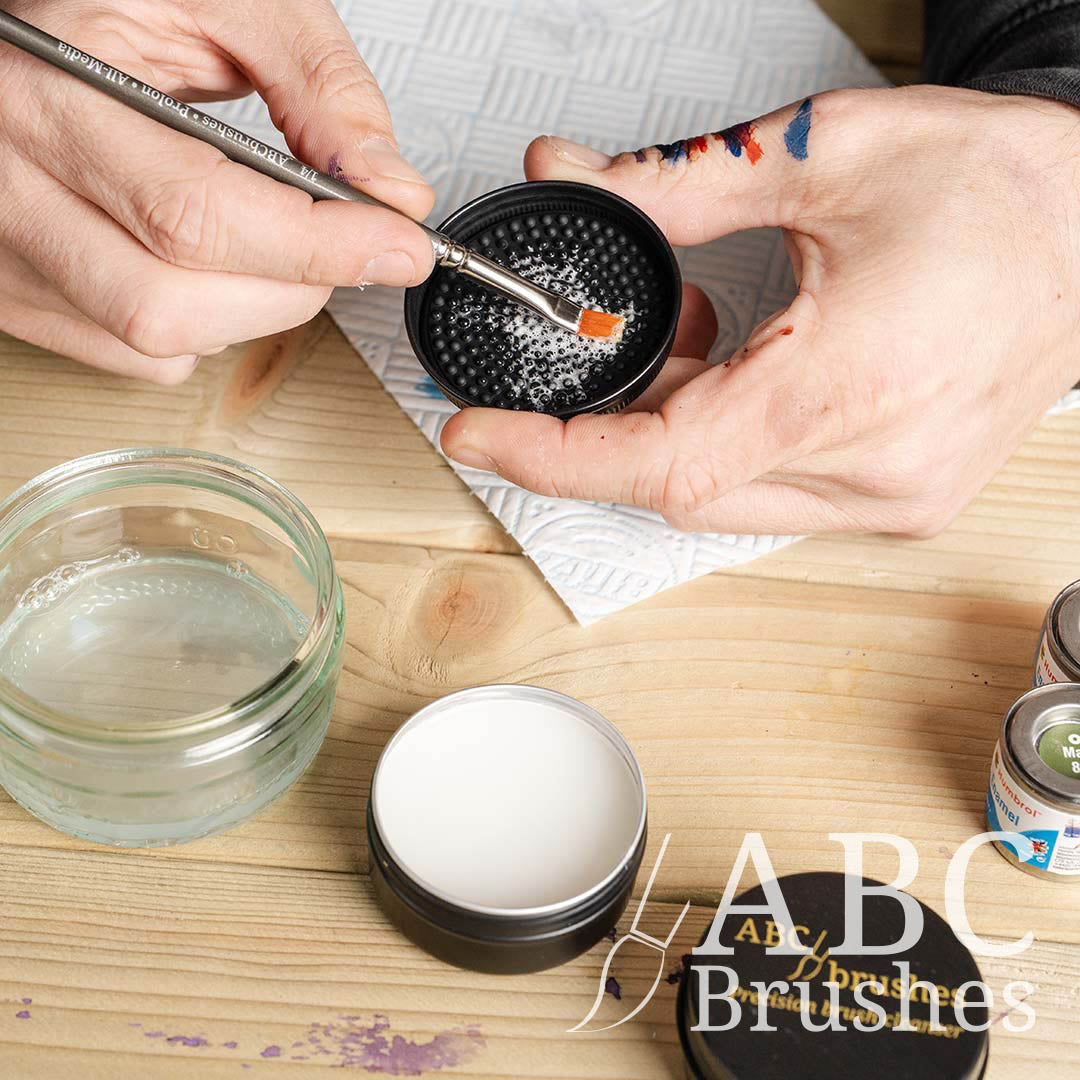 Someone cleaning a paintbrush with the textured lid of ABC Brushes brush cleaner.