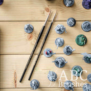 Two Pro Arte Imperium paint brushes on a wooden background surrounded by various painted and unpainted mini figures.