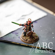 Fully painted armoured mini holding a green sword with a Pro Arte Imperium paint brush laid next to it. 