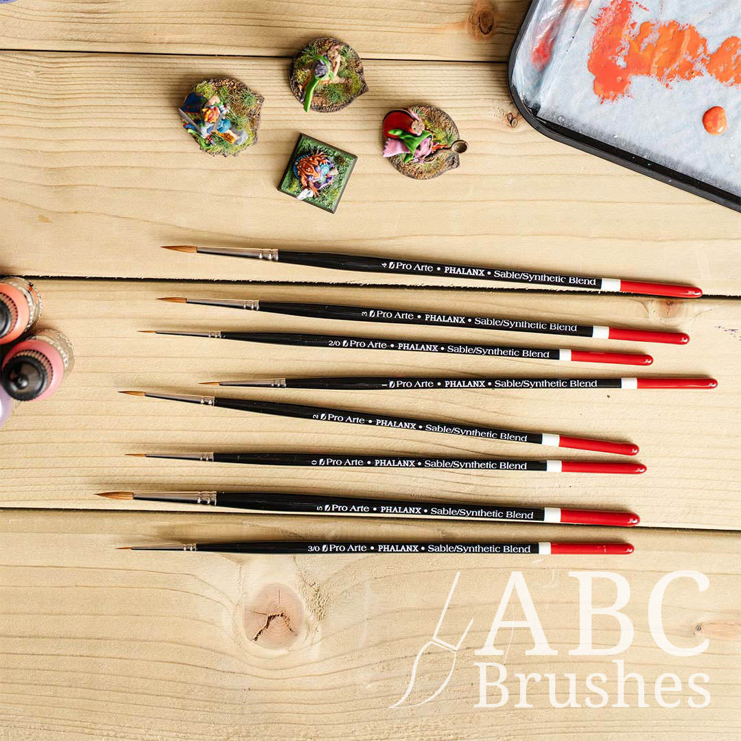 Pro Arte Phalanx round paint brush set laid out on a wooden background and with mini figures, paint bottles and a wet palette around them. 