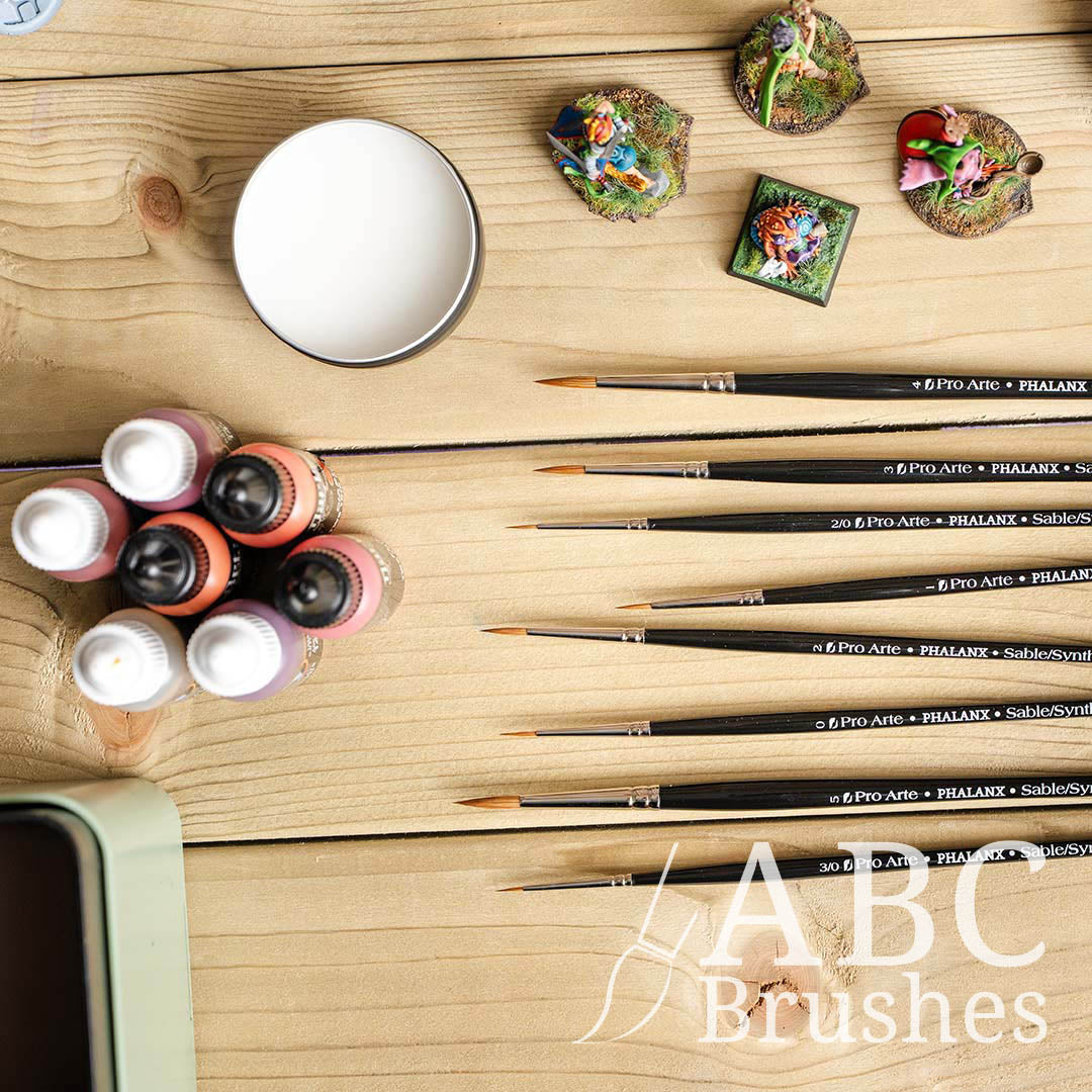 Pro Arte Phalanx round paint brush set laid out on a wooden background and with mini figures, paint bottles and Pro Arte brush cleaner around them. 