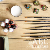 Pro Arte Phalanx round paint brush set laid out on a wooden background and with mini figures, paint bottles and Pro Arte brush cleaner around them. 