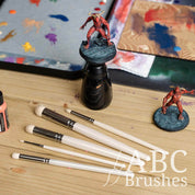 ABC Brushes Rounded Dry brush set next to a mini on a painting handle and various palettes. 