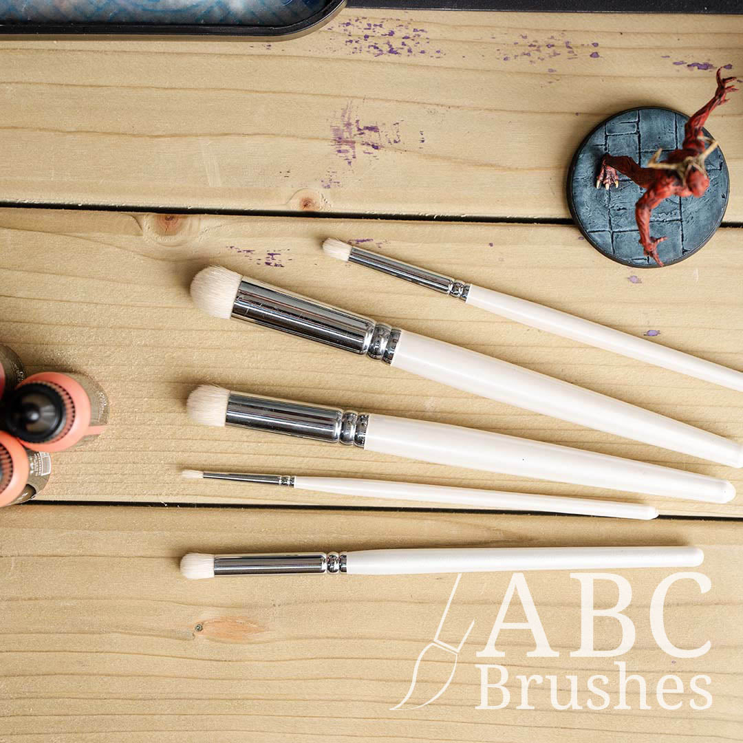 ABC Brushes Dry Brush set on a wooden background, next to acrylic paint bottles and a miniature. 