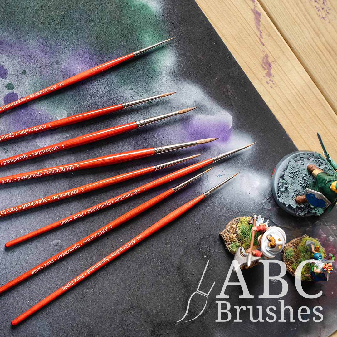 ABC Brushes Spearhead paint brush set laid out on a paint covered cutting mat and next to some painted minis.