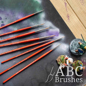 ABC Brushes Spearhead paint brush set laid out on a paint covered cutting mat and next to some painted minis.