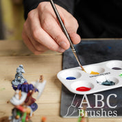 Person picking up yellow paint from an ABC Brushes paint palette. There are various miniature figures next to this.