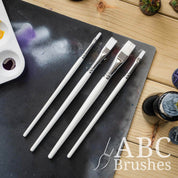 Pro Arte White Nylon flat paint brush set laid on top of a paint covered cutting mat. 