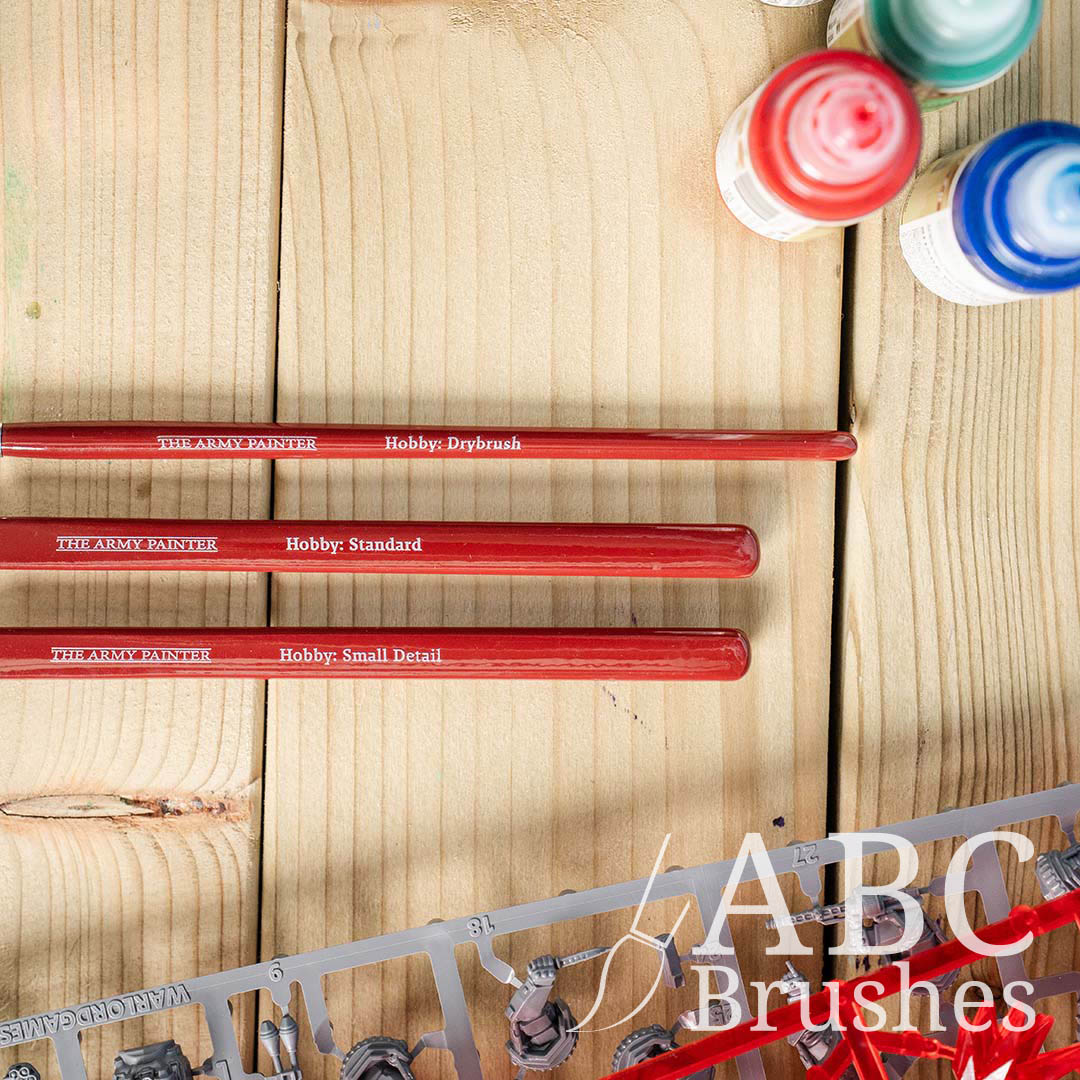 Closeup of the handles of the Army Painter Hobby Starter brush set next to a sprue and some acrylic paint bottles, on a wooden background.