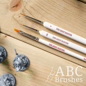 The Army Painter Most Wanted brush set on a wooden background, next to three miniature figures.